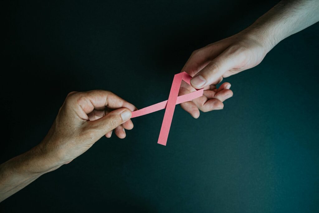 Two hands exchanging a pink ribbon symbolizing breast cancer awareness and support.